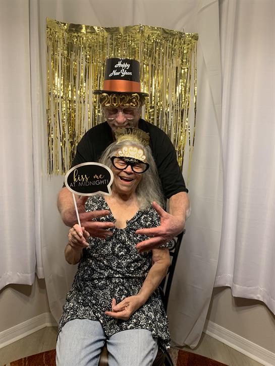An elderly couple is playfully posing with props at a lively party during a special celebration.