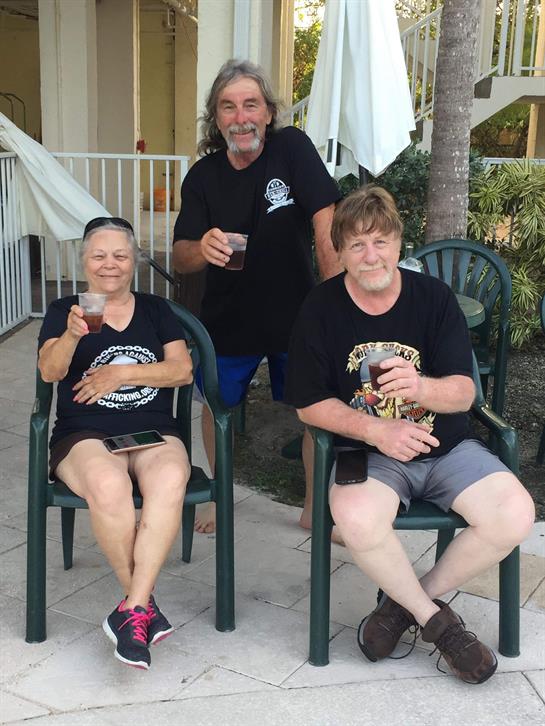 Three friends relax on chairs, sipping beverages and enjoying each other's company outdoors.