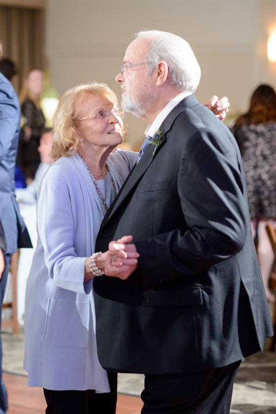 A joyful elderly couple dances closely together, enjoying the moment at a celebration.