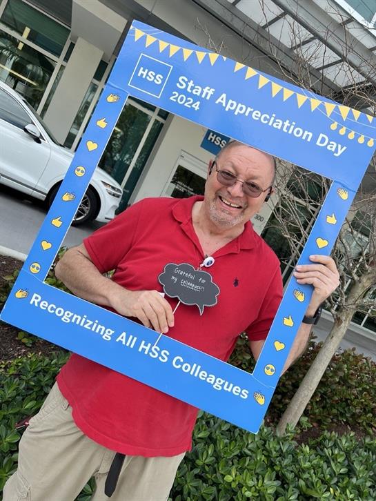 Individual celebrates staff appreciation day while posing with a recognition frame outside.