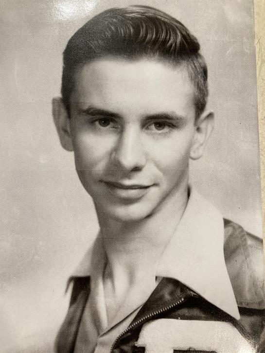 A young man with a charming smile poses in a classic 1950s black and white portrait.