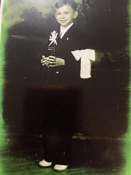 A young boy dressed in formal attire stands proudly, holding a decorative item in a classic setting.