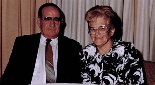 A cheerful elderly couple sits closely together, smiling warmly at a social event.