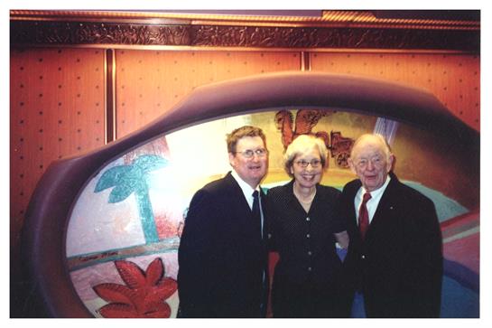 Portrait featuring three people smiling together in front of colorful artwork at an event.