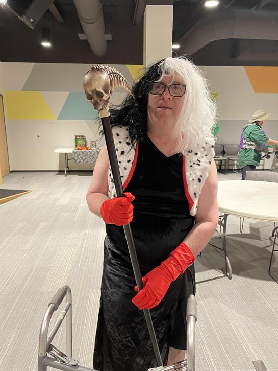 A person dressed in a dramatic costume holds a staff with a skull while standing indoors.