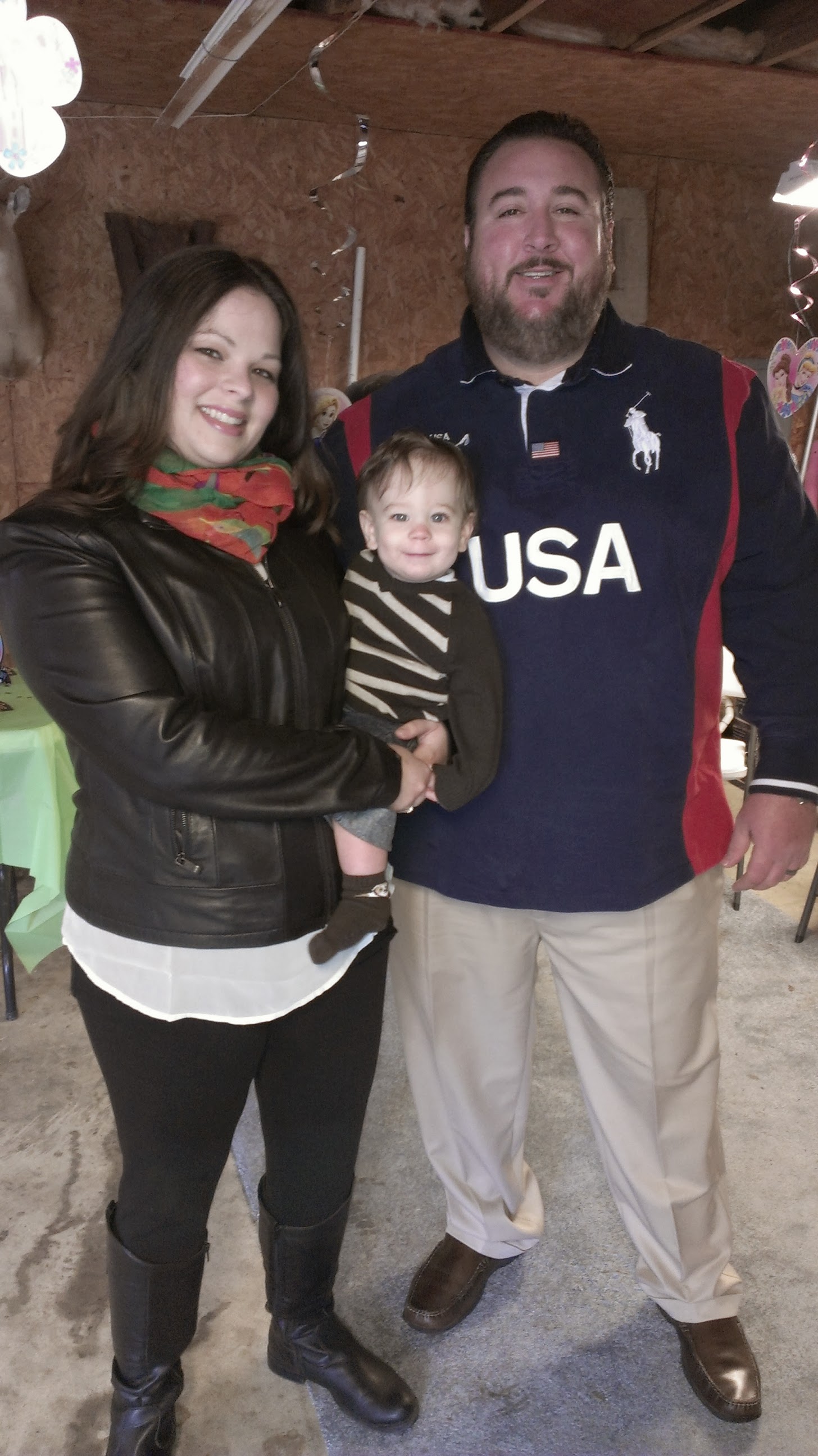 A woman holds a child while standing beside a man during a friendly family gathering indoors.