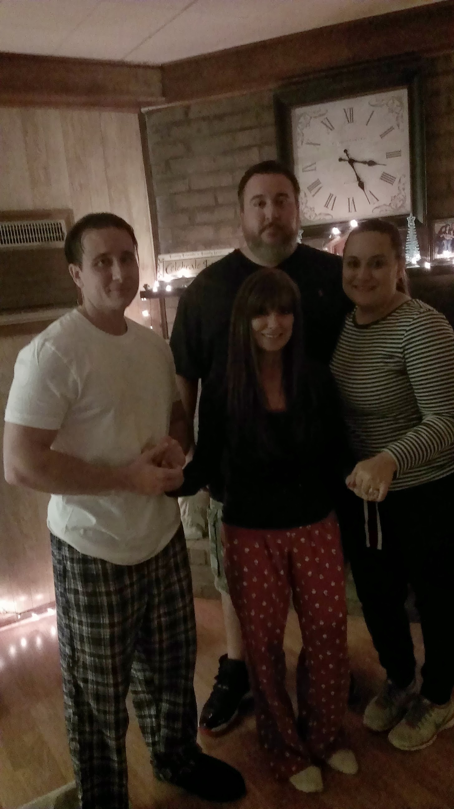 Four friends stand together in a warm indoor space with decorations and lights around them.