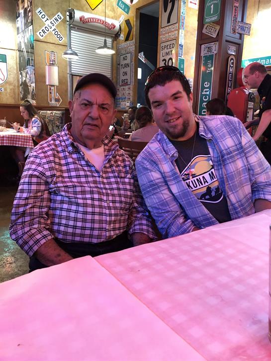 Two men smile while seated at a table in a warm, casual restaurant atmosphere.