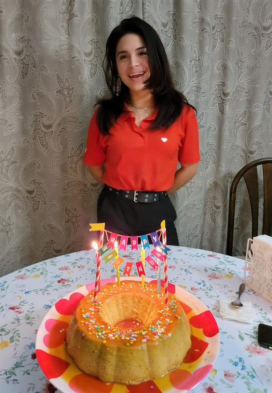 A young girl stands by a colorful cake adorned with candles and festive decorations.