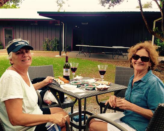 Women relax at a table outdoors, sharing snacks and wine while enjoying each other's company.