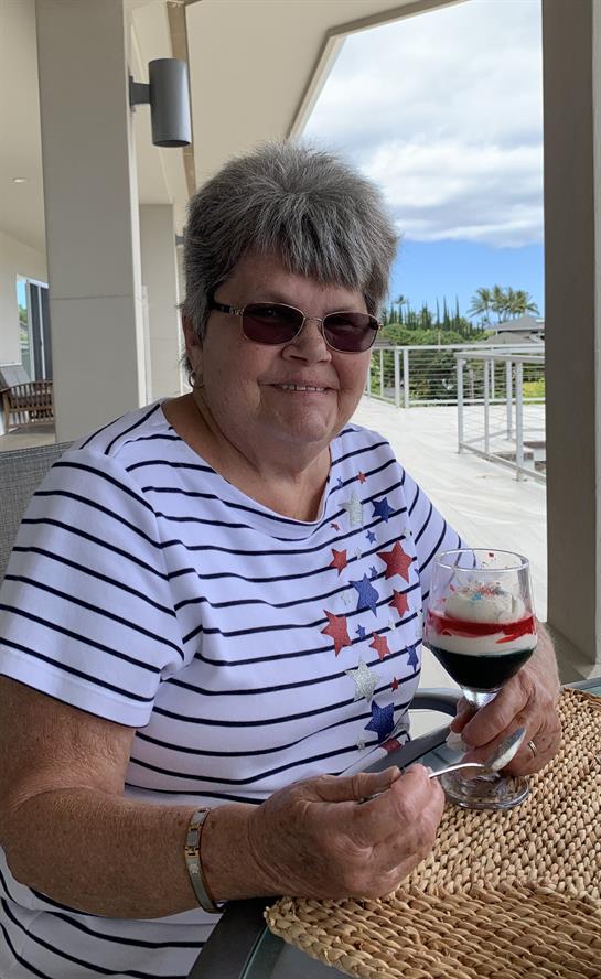 Gray-haired woman smiles outdoors with a berry dessert and whipped cream.