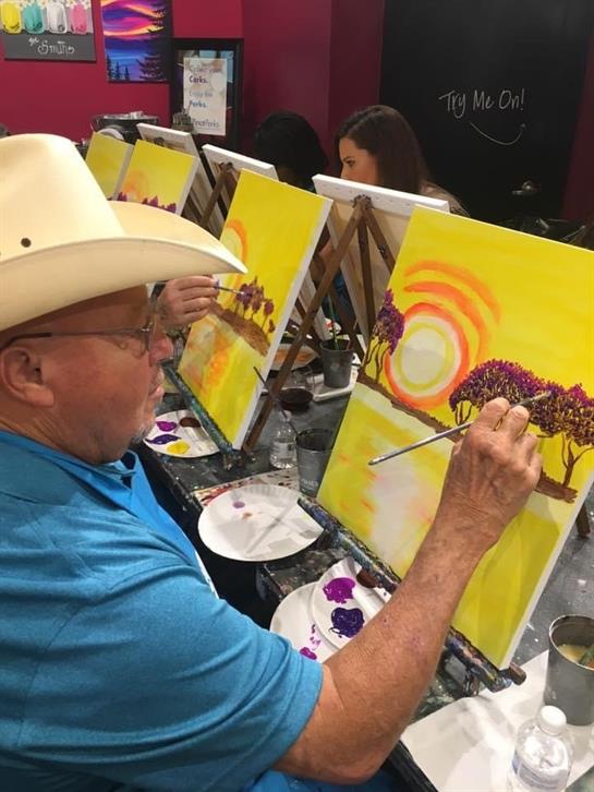 A group of seniors participates in a lively painting class, focusing on vibrant sunset landscapes.