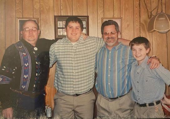 Four men share smiles and style in a cozy, wood-paneled room.