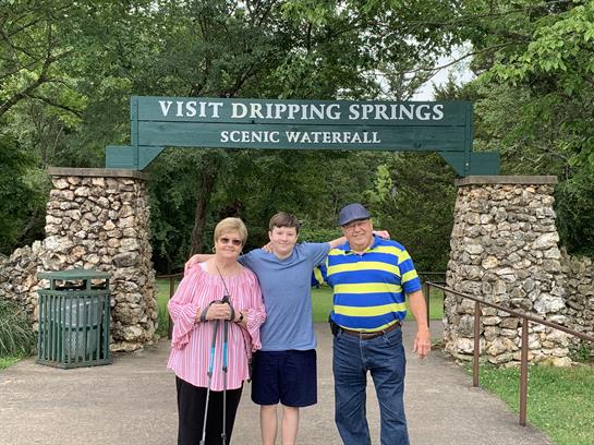 Family poses together at the entrance to Dripping Springs waterfall, enjoying a sunny day outdoors.