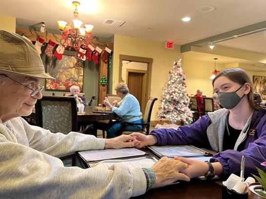 A man and a young woman hold hands at a table in a festive dining area during winter.