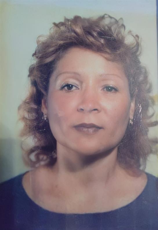 A woman with curly hair poses for a portrait, wearing a blue dress and natural makeup, indoors.
