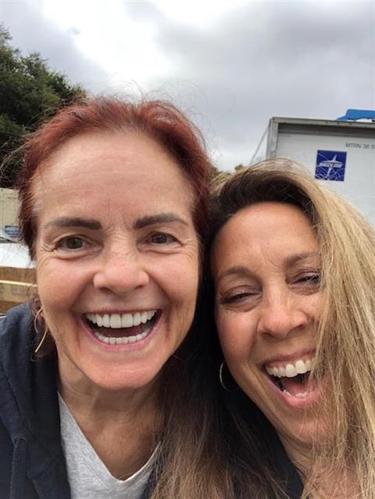 Two smiling friends enjoy a lighthearted moment outdoors under cloudy skies.