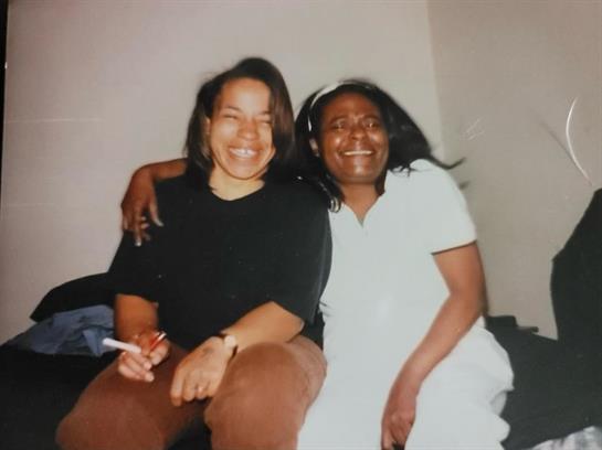 Two women sit close, smiling and enjoying each other's company in a cozy room.