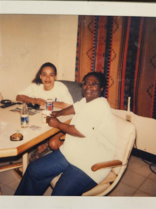 Two women sit at a dining table together, sharing conversation and snacks in a warm environment.