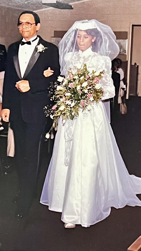 A bride in a lovely white gown walks with her father, holding a bouquet at the wedding.