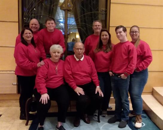 Nine individuals wearing red sweaters gather in a hotel lobby for a festive family reunion.