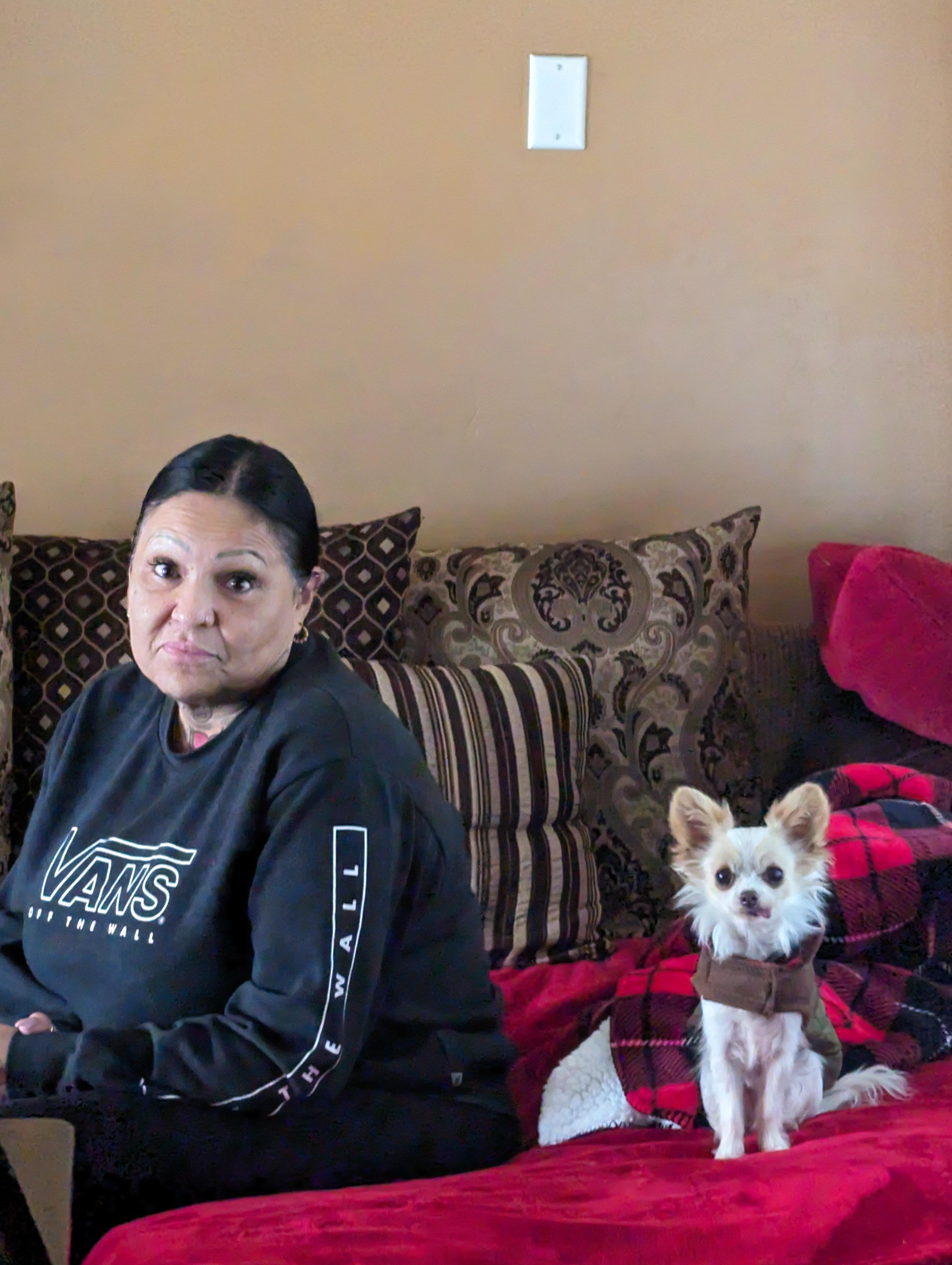 A woman and her small dog relax together on a couch surrounded by pillows and blankets.
