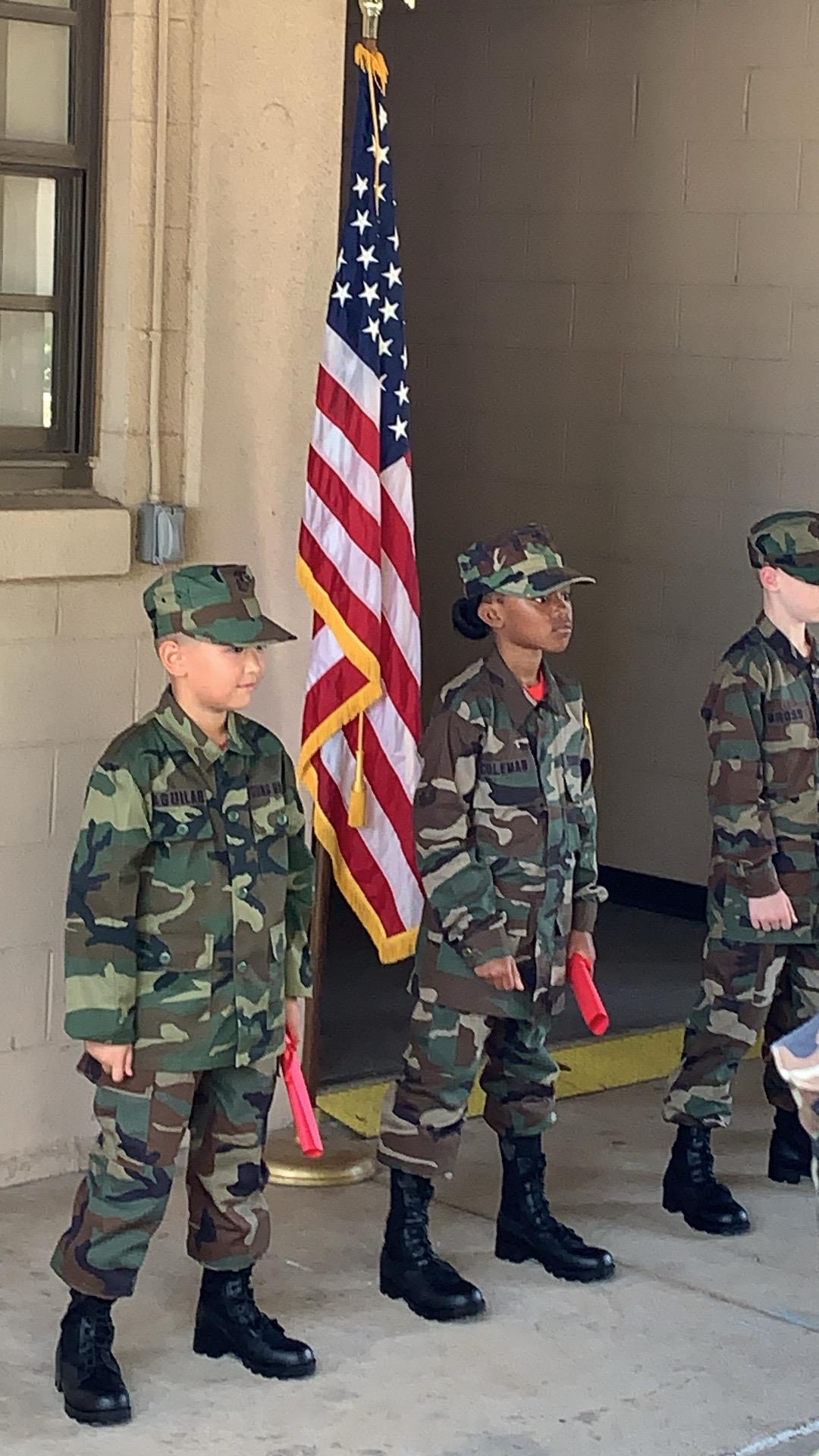 Cadets dressed in military attire stand in formation, holding flags, ready for a ceremony.