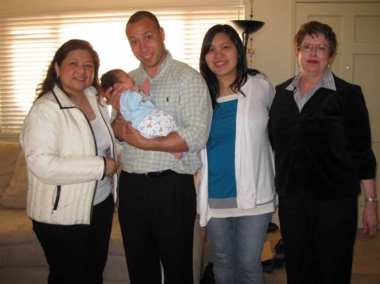 A father holds his newborn baby surrounded by family members in a cozy living room.
