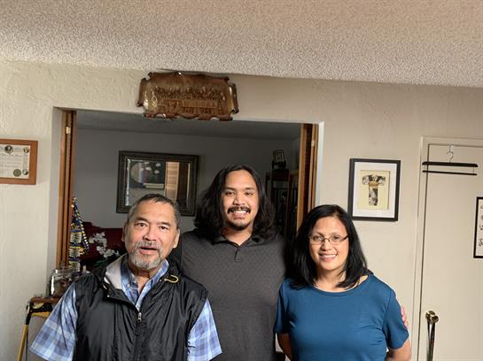 Three family members pose together in a warm and inviting living room, smiling happily.