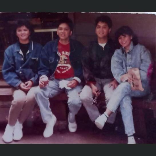 Four friends relax on a bench, dressed in denim, enjoying drinks and a friendly chat.