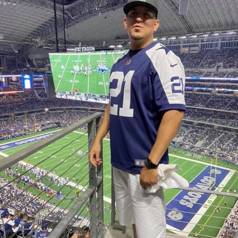 Enthusiastic fan wearing a team jersey stands in an upper section of a vibrant stadium.
