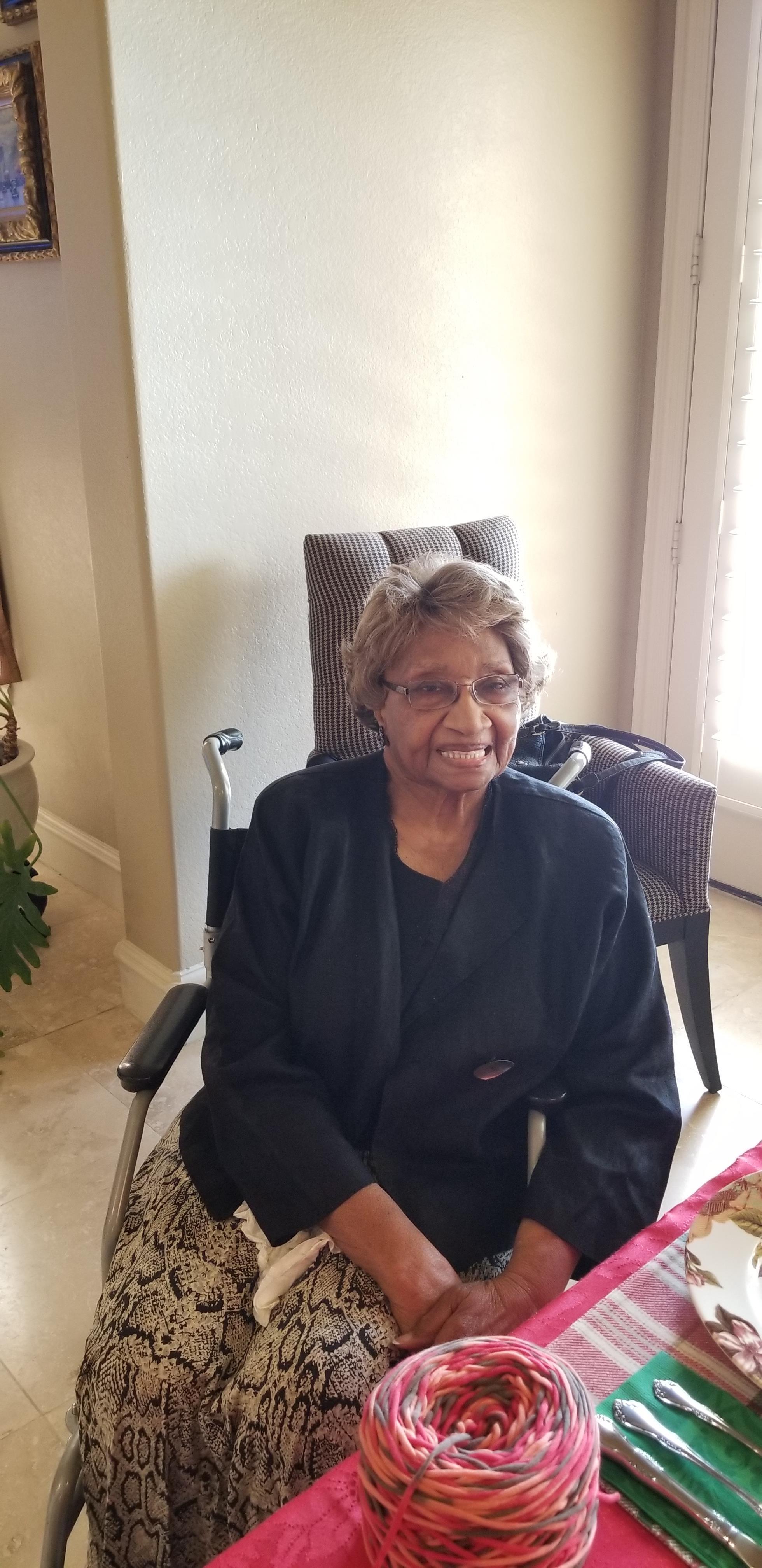An elderly woman enjoys a cheerful moment in a bright room, seated comfortably in a chair.