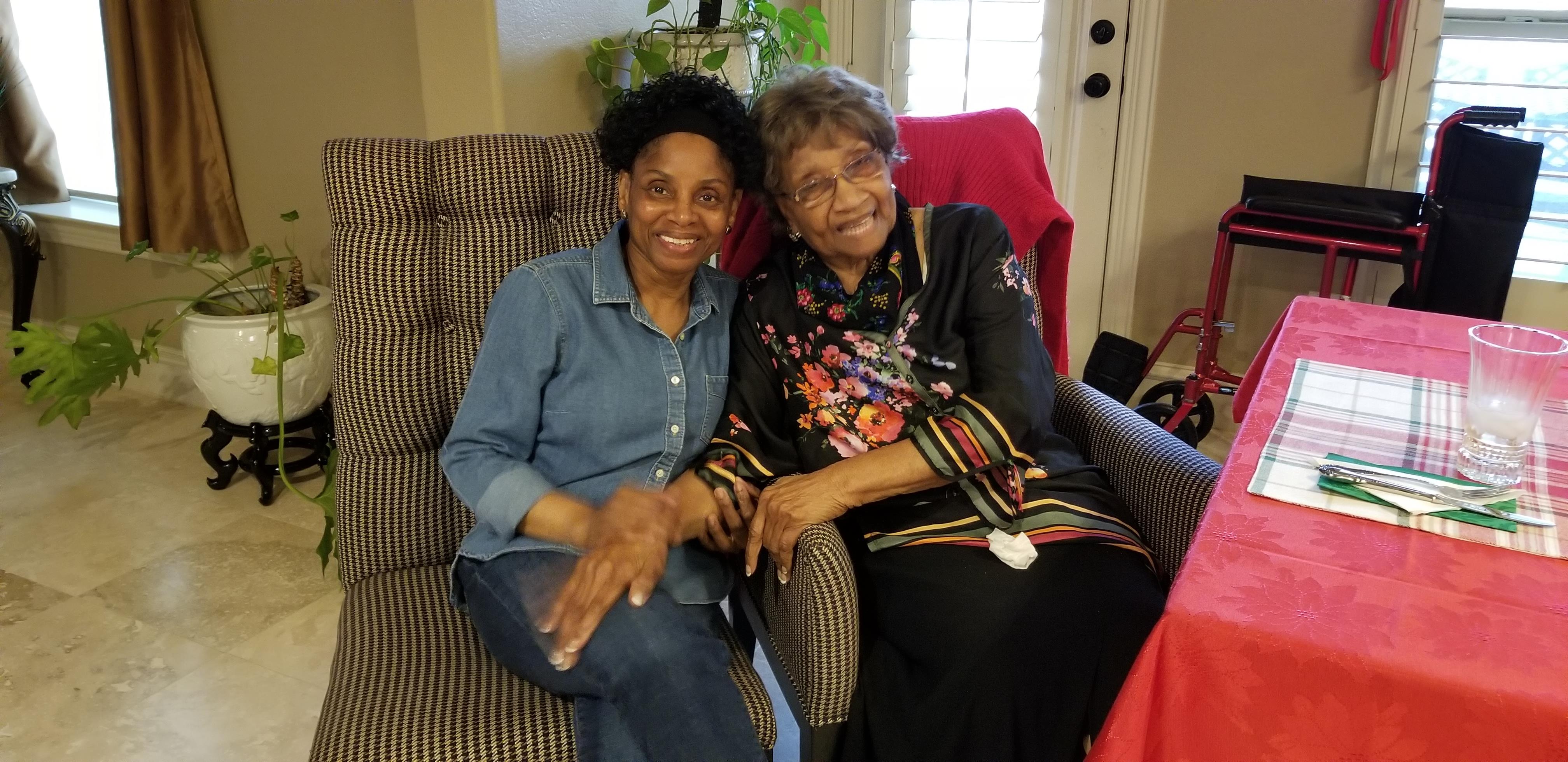 Two women sit closely together, smiling and enjoying each other's company in a warm setting.