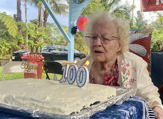 An elderly woman at her 100th birthday party prepares to blow out candles on a cake.
