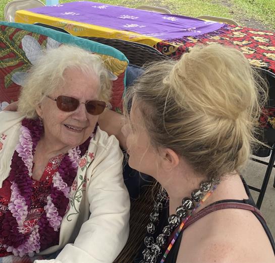 Two women share smiles during a joyful moment at a vibrant outdoor celebration.