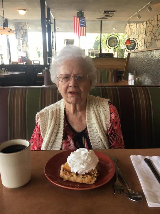 An elderly woman sits at a table, savoring dessert topped with whipped cream alongside her coffee.