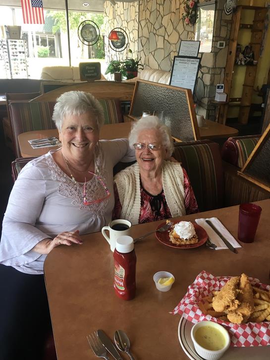 Two elderly women share a joyful moment over breakfast with delicious food in front of them.