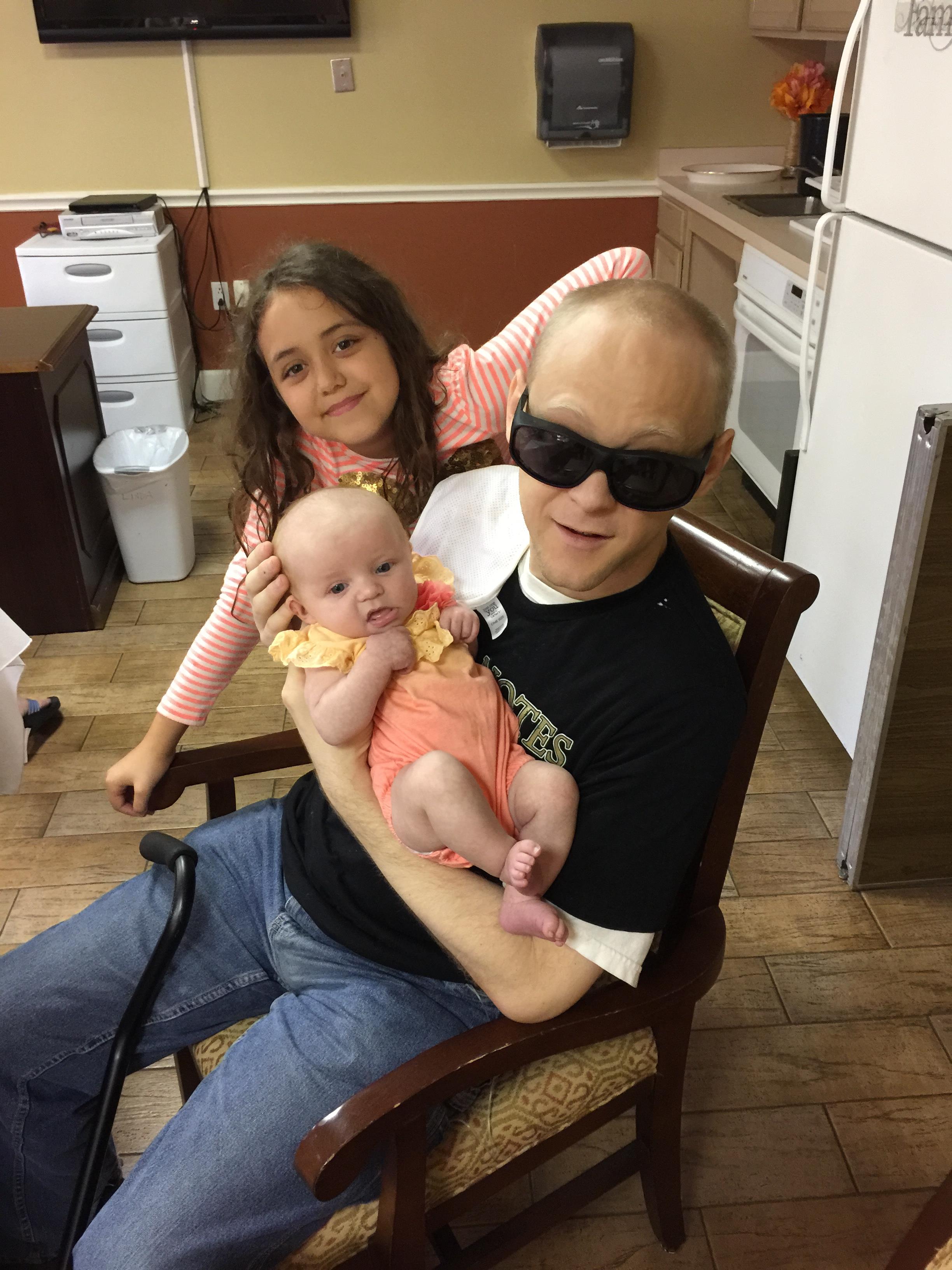 A joyful moment featuring a man with sunglasses holding a baby while a girl sits behind him.