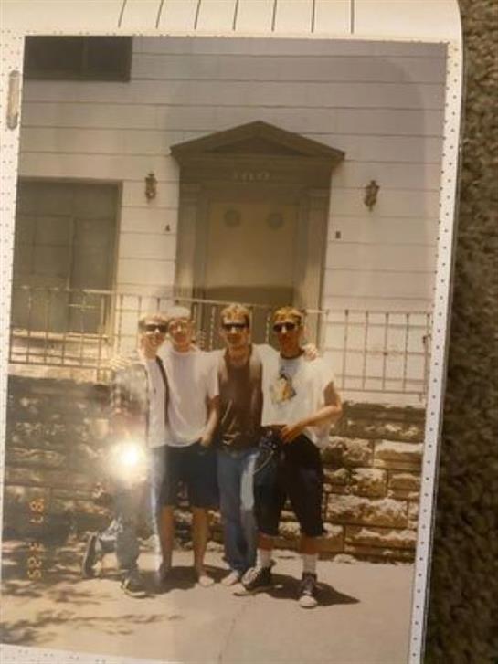 Four friends stand side by side, smiling in front of an old building, enjoying their time together.