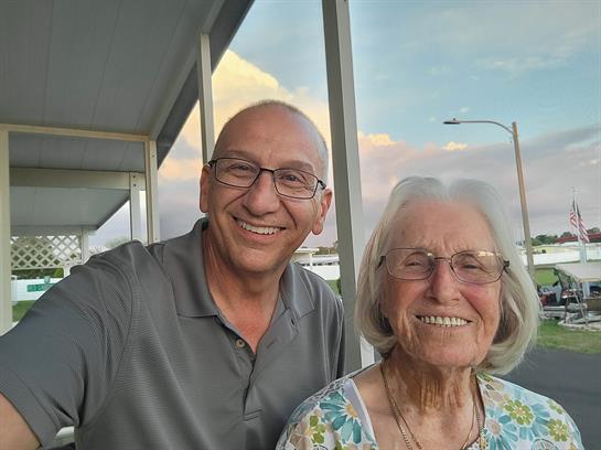 A man and an elderly woman sit together on a porch, smiling and enjoying each other's company.