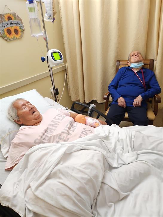 A man lying in a hospital bed next to a man in a chair