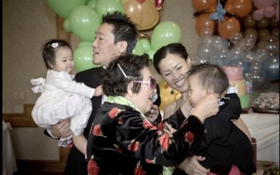 Family members joyfully interact at a celebration, carrying little ones and sharing laughter.