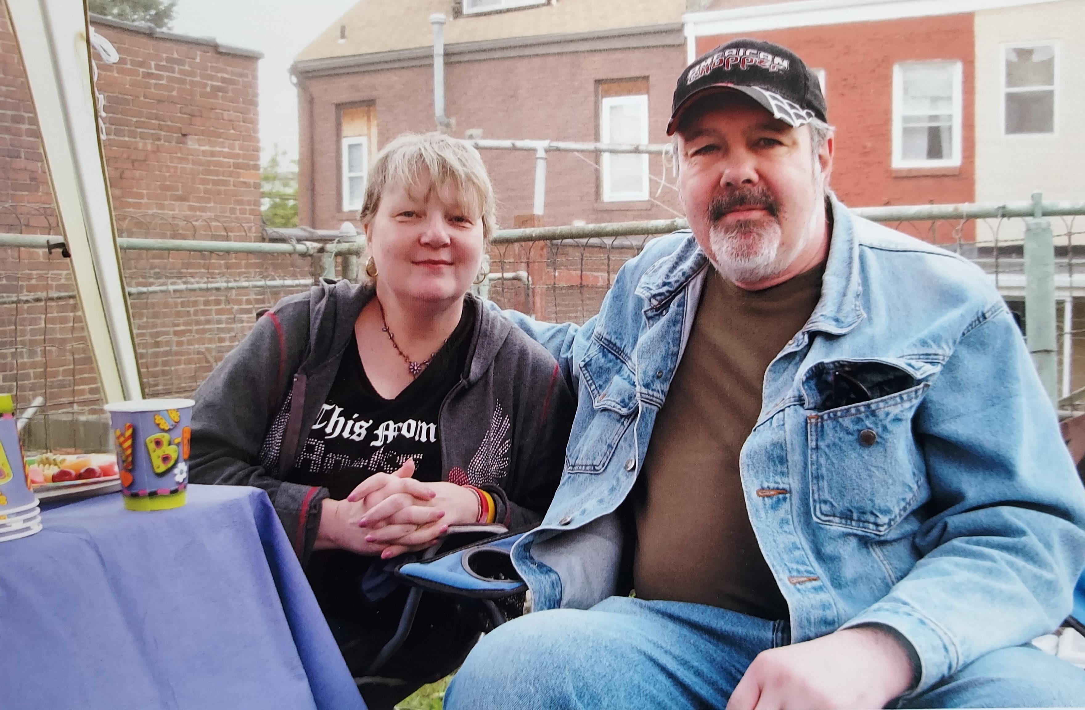 A couple is seated comfortably at a casual gathering, smiling and enjoying each other's company.