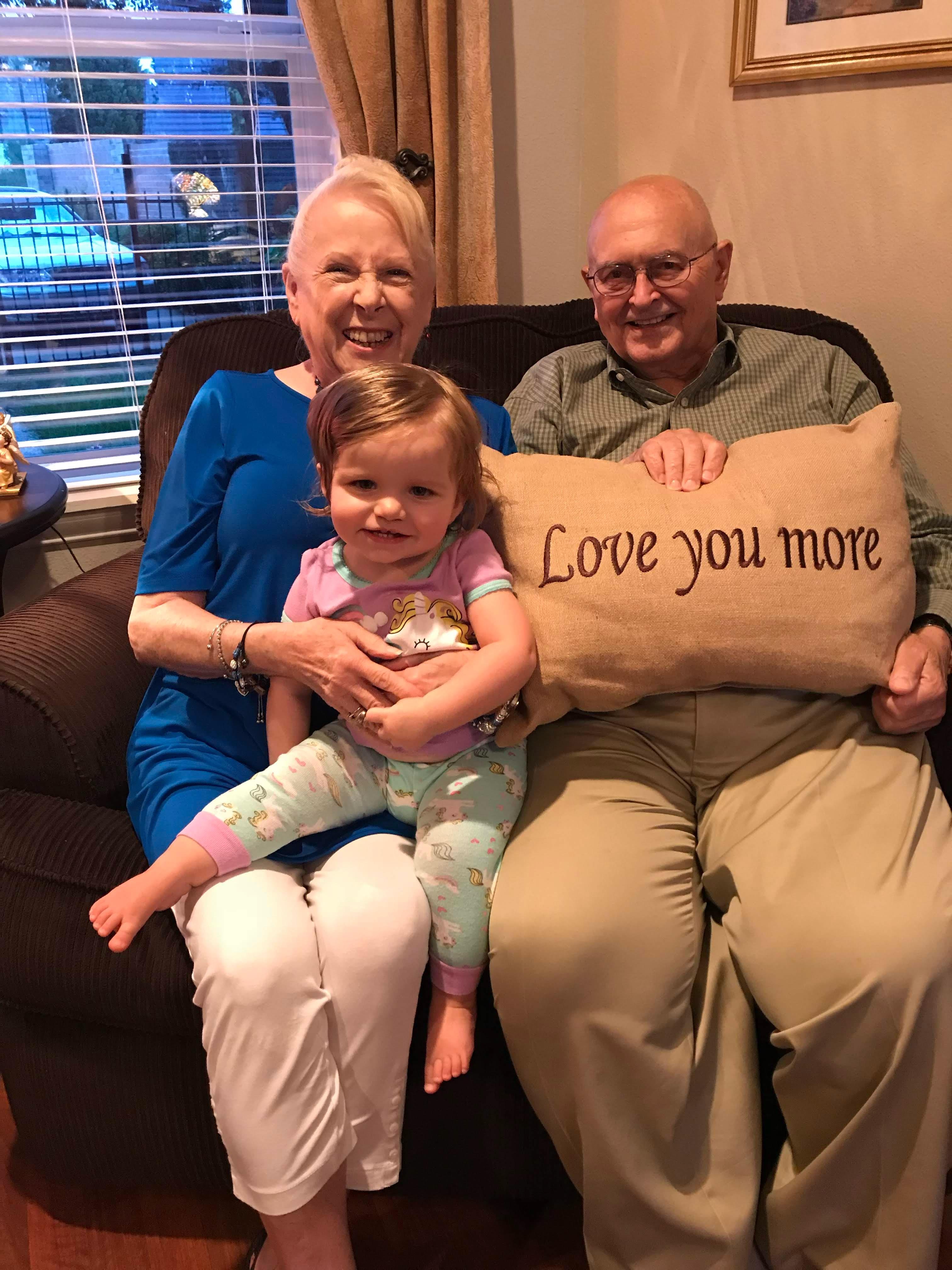Grandparents sit together on a couch with their granddaughter, displaying a loving family bond.