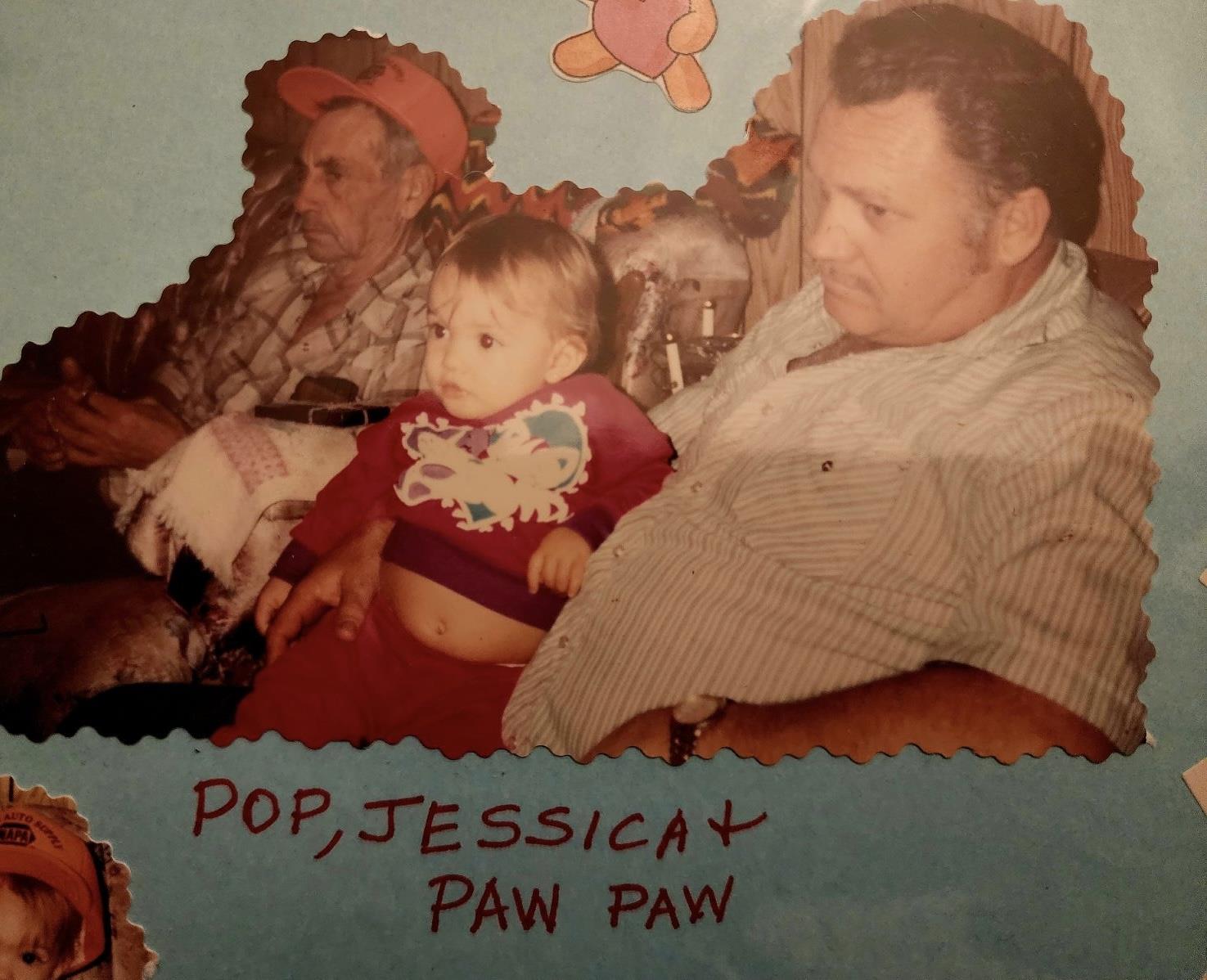 Two older men and a toddler share a moment on a couch, surrounded by decorations and toys.