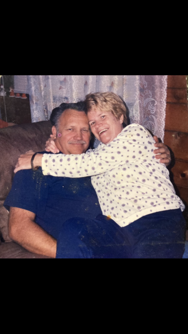 Man and woman share a warm embrace while sitting comfortably on a couch inside their home.