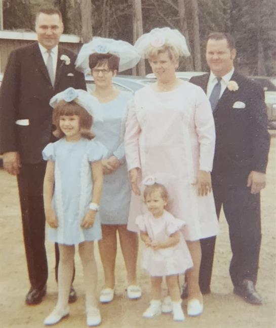 A family in formal wear poses together at a wedding celebration outdoors in the countryside.