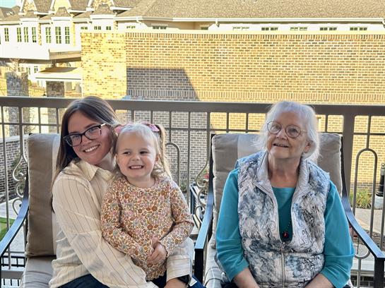 Three generations are happily sitting together on a balcony, sharing smiles and laughter.