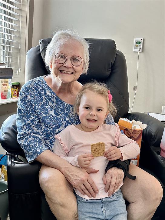 Loving embrace between grandmother and granddaughter in a comfortable chair, sharing smiles.