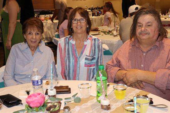 Three relatives enjoy a festive gathering at a banquet table filled with beverages and desserts.